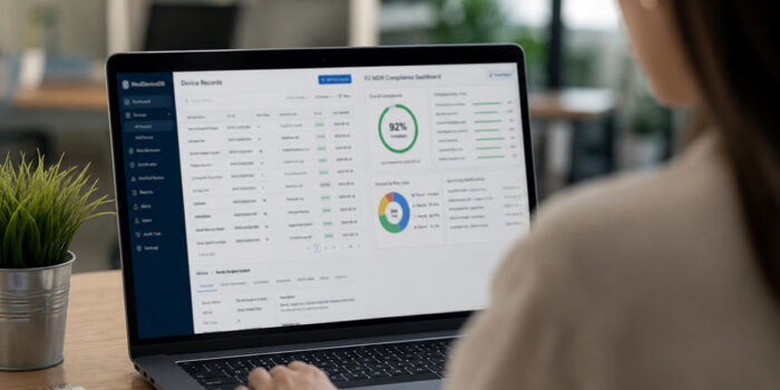 Regulatory affairs specialist reviewing a medical device compliance dashboard on a laptop, showing EU MDR compliance scores, UDI device records and certification status — illustrating mandatory EUDAMED registration for manufacturers.